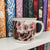 Locked Tomb mug with skull design on a shelf with colourful books image