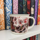 Locked Tomb mug with skull design on a shelf with colourful books
