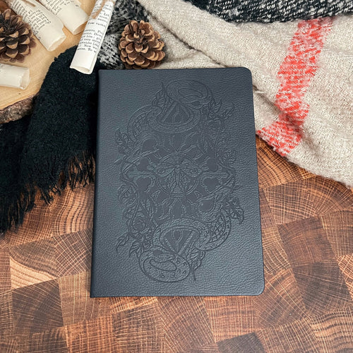 Dark notebook with embossed design on a wooden surface with pine cones and books. image