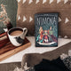Illumicrate edition of Nimona by ND Stevenson leaning against a brown cushion, next to a mug of coffee and a book stack.