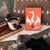 Nimona Illumicrate Exclusive foil hardcover displayed against a brown cushion, next to a mug of coffee. image